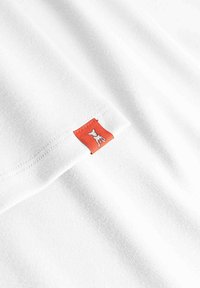 Biały materiał z małą czerwoną metką wszytą na krawędzi, z białym konturem stojącego psa.