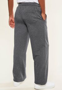 Graue Sweatpants aus weichem Material mit elastischem Bund, seitlichen Taschen und lockerer Passform, kombiniert mit weißen Sneakers.