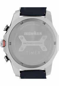 Sidabrinis nerūdijančio plieno laikrodžio korpusas su mėlynu silikoniniu dirželiu. Nugarėlėje yra išgraviruotas tekstas, įskaitant "IRONMAN" ir "TIMEX", taip pat akumuliatoriaus modelis.