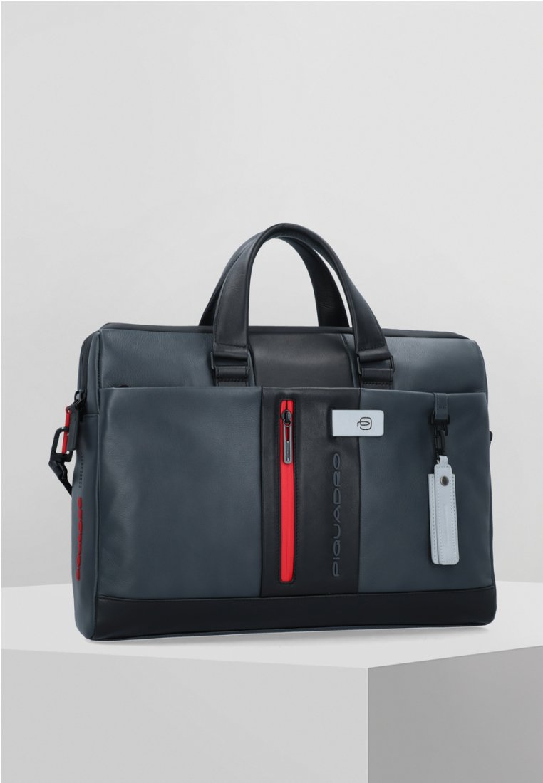 Bolso de cuero azul oscuro con acentos en cremallera roja, dos asas superiores y un parche de logo en la parte frontal. Incluye una etiqueta removible y una superficie texturizada.