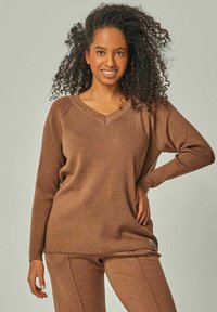 Brauner Strickpulli mit V-Ausschnitt und gerippter Textur. Hat überschnittene Schultern und eine lockere Passform. Wird mit passenden Hosen kombiniert.