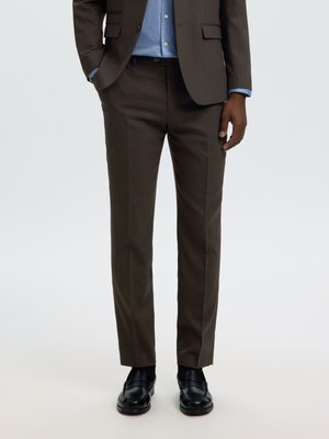 Homme portant un pantalon de costume marron foncé sur mesure, une veste de costume assortie, une chemise bleu clair et des chaussures en cuir noir.