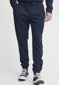 Marineblauwe sweatpants met een elastische tailleband en trekkoord; zachte textuur; voorzien van twee frontzakken en boorden aan de enkels. Gekoppeld met zwarte sneakers.