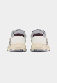 Paire de baskets blanches et grises avec semelles beiges vues de dos sur un fond clair uni.