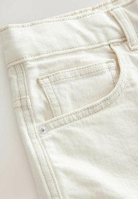 Weiße Jeans verfügen über eine Fronttasche mit weißer Naht und einem Metallnieten, die eine strukturierte Stoffoberfläche zeigt.