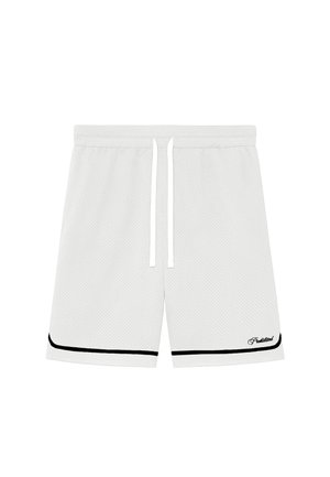 Męskie nogi w białych siateczkowych szortach z czarnym obszyciem, białe skarpetki z napisem „Prohibitions” oraz jasnobrązowe mokasyny na neutralnym tle.