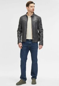 Giacca di pelle, grigio scuro, con zip frontale e due tasche sul petto. Abbinata a jeans blu e sneakers verde oliva.