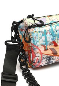 Flerfärgad tygpåse med ett strukturerat mönster, med svart kedja och justerbar rem. Två blixtlåsfickor synliga.