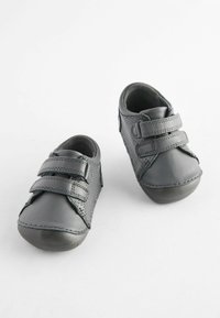 Chaussures en cuir gris avec des côtés perforés et deux sangles Velcro ajustables. Bout rond et semelles en caoutchouc flexibles pour la stabilité.