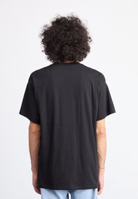 T-shirt en coton noir à manches courtes et col rond, présentant une texture lisse et une coupe décontractée, vue de l'arrière.