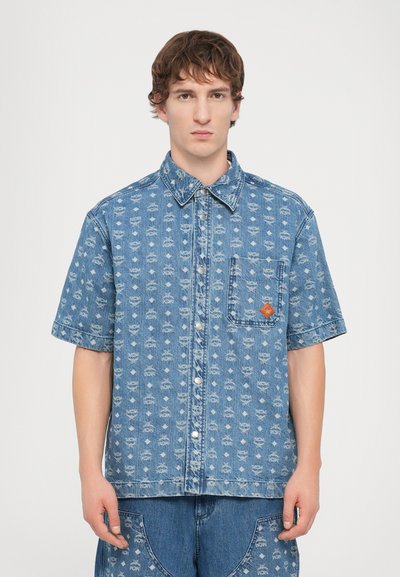 Camicia di jeans a maniche corte in azzurro chiaro con un motivo ripetuto, bottoni a pressione, taschino sul petto e un patch con logo arancione a contrasto.