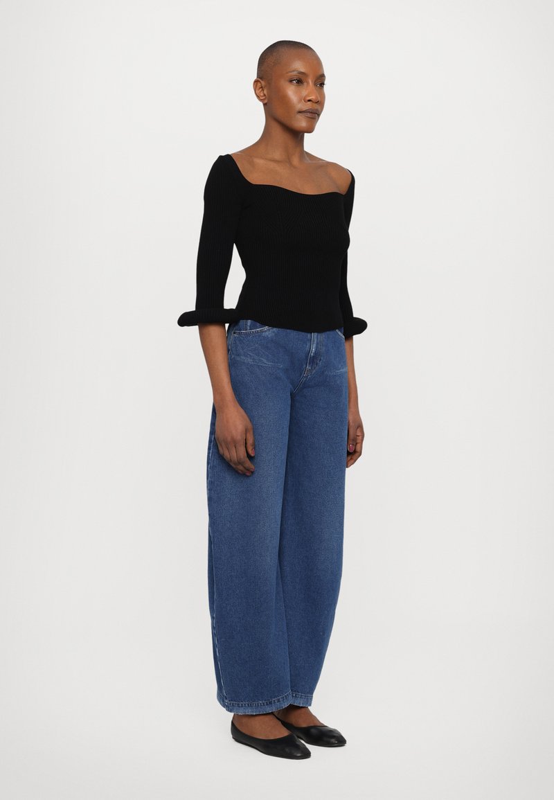 Black ribbed top with off-shoulder design and three-quarter sleeves; paired with wide-leg blue denim jeans and black flats.