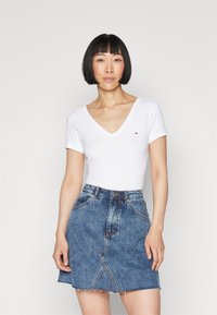 Hvit kortermet V-hals topp parret med en blå jeans A-linje mini skjørt med frynset kant og kontrastsøm.