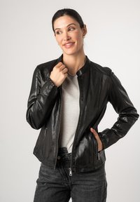 Schwarze Lederjacke mit rundem Kragen, Reißverschluss und zwei Seitentaschen. Glatte Textur und taillierte Passform. Trägt man über einem grauen Oberteil.