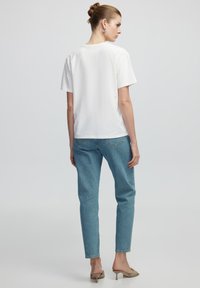T-shirt bianca a maniche corte abbinata a jeans in denim azzurro chiaro. I jeans presentano un design a vestibilità dritta e cuciture a contrasto.