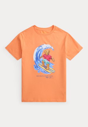Camiseta de manga corta naranja con un dibujo de un oso surfeando una ola y el texto "Polo Bear by Ralph Lauren" debajo.