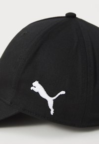 Căciulă neagră dintr-un material texturat, cu un logo Puma brodat alb. Formă rotundă, cu un buton cusut în vârf și curea ajustabilă.
