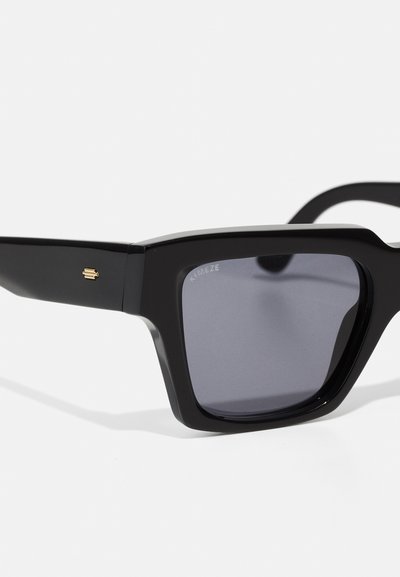 Μαύρα γυαλιά ηλίου με χοντρό τετράγωνο σκελετό και γκρι φακούς. Διαθέτουν μία μικρή χρυσή λεπτομέρεια στο πλάι και γυαλιστερή επιφάνεια.
