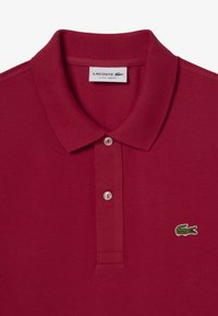 Polo slim fit de Lacoste en rojo con cuello, dos botones blancos y logo de cocodrilo verde en el pecho.