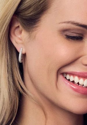 Silverhoopsörhängen med en slät, polerad yta och spridda små detaljer som liknar ädelstenar, buren på en modell.