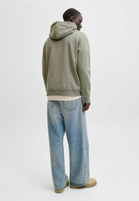 Vihre�ä huppari rentolla istuvuudella, yhdistetty vaaleansinisiin leveälahkeisiin farkkuihin. Sileä pinta, säädettävä huppu ja hillityt ompeluominaisuudet.