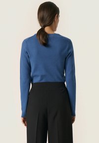 Blaues Langarmshirt mit rundem Halsausschnitt, strukturiertem Strickstoff, kombiniert mit hochtaillierten schwarzen Hosen mit glatter Oberfläche.