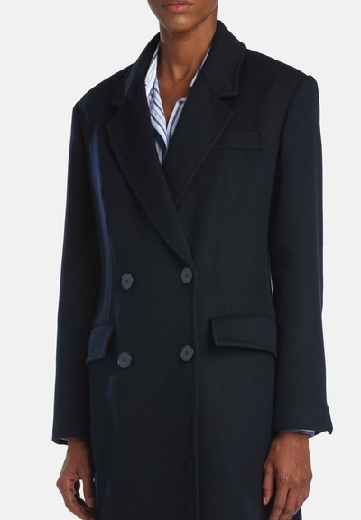 Manteau bleu marine en laine à double boutonnage avec de grands boutons noirs, revers crantés et poches latérales. Texture lisse avec une coupe ajustée.