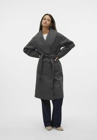 Abrigo gris de mezcla de lana con cuello de chal, diseño envolvente y cinturón, combinado con jeans de pierna ancha azul oscuro y zapatos de punta beige.