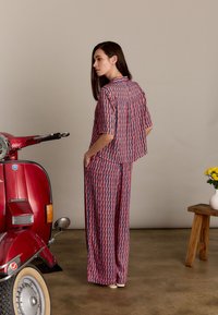 Twee-delig outfit bestaande uit een top met korte mouwen en een broek met wijde pijpen in een rood en marineblauw geometrisch patroon. Glad materiaal, ontspannen pasvorm.