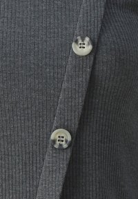 Cardigan gris en tricot côtelé avec deux boutons transparents à quatre trous chacun et un détail de fermeture à un bouton.