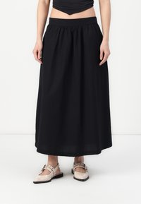 Svart lang skjørt laget av lett stoff, med en rynket midje og en flytende silhuett, kombinert med blush flate sko.