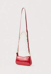 Mala de mão em pele vermelha de verniz com uma correia longa ajustável e detalhe em corrente, apresentando um fecho de correr e uma textura lisa e brilhante.