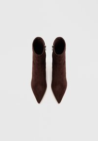 Botas de ante marrón hasta el tobillo con punta afilada, que cuentan con un cierre de cremallera en el lateral. Textura suave y diseño estilizado.