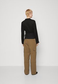 Bluză neagră cu mânecă lungă, cu guler volant și detaliu de cravată la spate, asortată cu pantaloni cargo bej, cu buzunare laterale.
