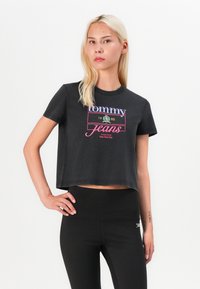 Černé zkrácené tričko s barevným potiskem loga "Tommy Jeans" a datem založení. Krátké rukávy a měkký bavlněný materiál.