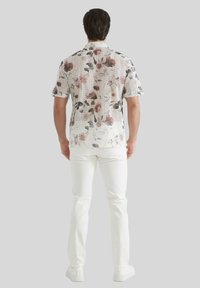Chemise à manches courtes à motifs floraux avec une base blanche ornée de motifs floraux roses et foncés, accompagnée d'un pantalon blanc et de chaussures décontractées.
