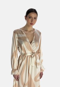 Robe portefeuille à manches longues en beige clair avec un tissu fluide. Présente un décolleté en V, une taille ceinturée et des motifs abstraits en vagues crème et taupe.