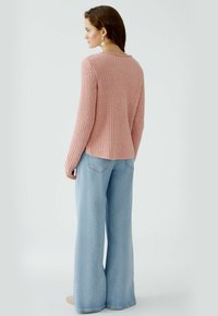 Rosa gerippter Pullover mit langen Ärmeln, rundem Ausschnitt und lockerer Passform, kombiniert mit hellblauen Schlagjeans, die über Gesäßtaschen verfügen.