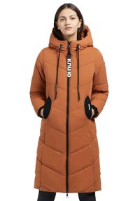 Lång, fluffig orange kappa med huva, med en svart dragkedja, triangulär quiltning och svarta sidofickor med detaljer.