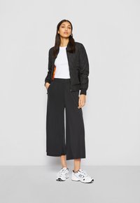 Mustapintainen podar jacket, jossa on oranssi vuori, yhdistettynä löysiin mustiin culotteihin ja valkoisiin lenkkareihin. Alla yksinkertainen valkoinen T-paita.