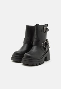 Black leather ankle boots featuring a chunky sole, strap details, and buckle accents. Smooth texture with a rugged, treaded outsole.