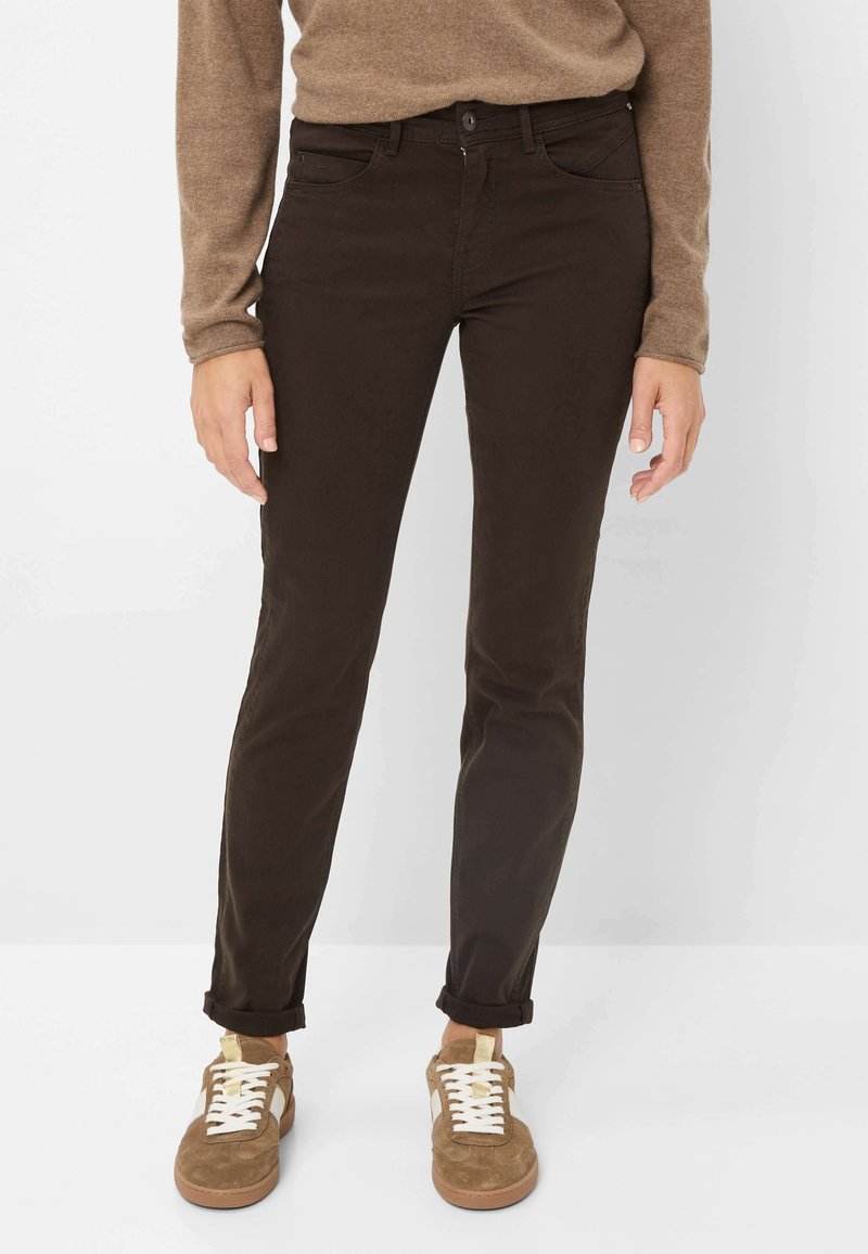 Brune bomuldsjeans med lige pasform, der har forlommer og knaplukning. Matchet med brune sneakers og en beige sweater.