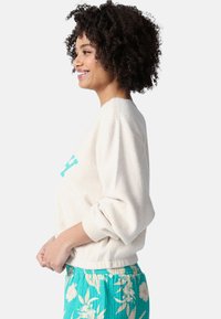 Sudadera de felpa relajada en color crema con mangas oversized, que presenta un gráfico en turquesa; combinada con pantalones cortos de estampado floral en verde menta.