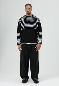 Zwart-wit gestreept shirt met lange mouwen en een ronde hals, gecombineerd met losse zwarte broek en zwarte schoenen met contrasterende veters.