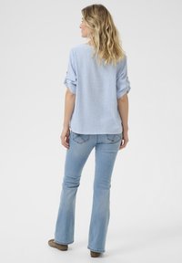 Ribaga sinine ja valge pluus keeratud varrukatega, koos heledate denimite lahtiste pükstega. Mudel on veidi vasakule poole, näidates selja detaile.