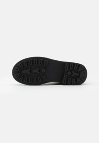 Suela de bota de goma negra con un patrón de relieve texturizado, que presenta diseños hexagonales y en forma de flecha para proporcionar tracción. Bordes lisos.