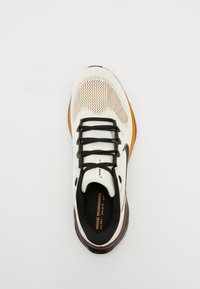 Vue de dessus d'une chaussure de course Nike blanche et noire avec des touches orange et des lacets noirs sur un fond uni.