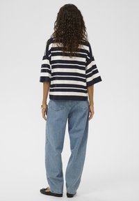 Gestreiftes, kurzes Oberteil aus marineblauem und weißem Baumwollstoff, kombiniert mit lockeren, hellblauen Jeans. Getragen mit schwarzen flachen Schuhen und einem goldenen Armband.