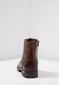 Bottine en cuir marron à texture lisse, avec une fermeture éclair à l'arrière et des coutures renforcées. Semelle en caoutchouc noir solide, design minimaliste.