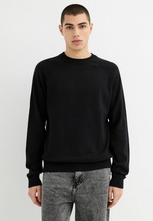 Suéter negro con cuello redondo, puños y dobladillo acanalados. Hecho de un material suave con una textura lisa, cuenta con mangas raglán para un ajuste relajado.